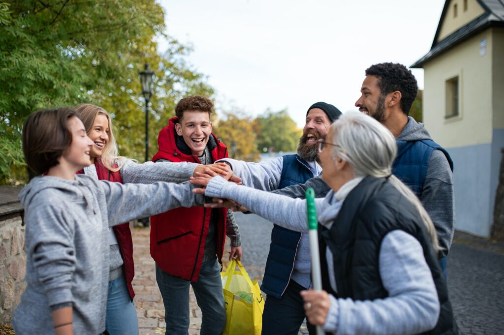 Diverse group of happy community service volunteers stacking hands together outdoors in street