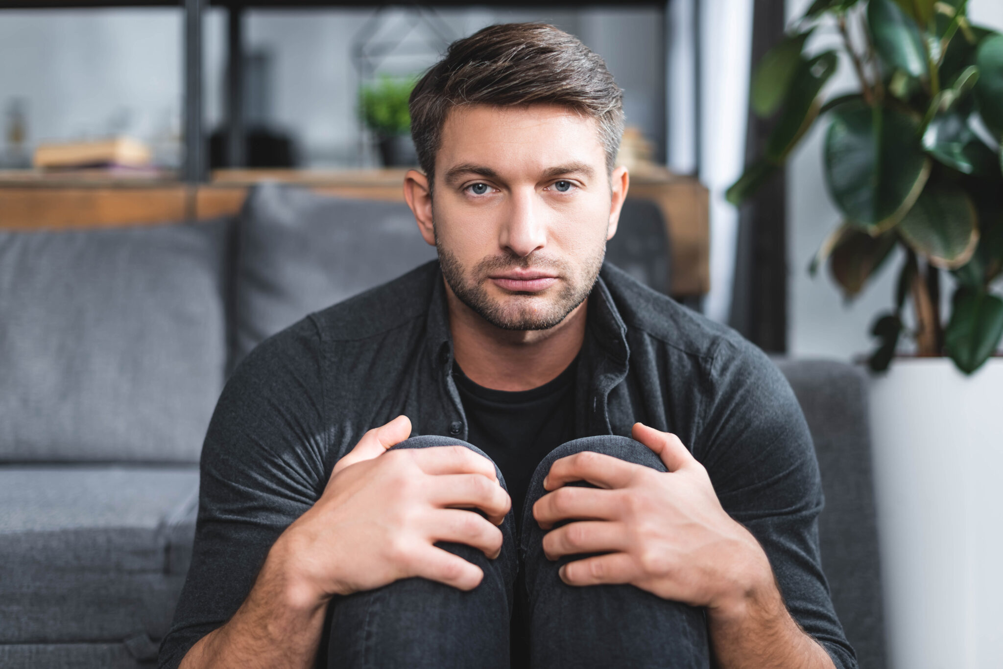 handsome man with panic attack hugging legs in apartment