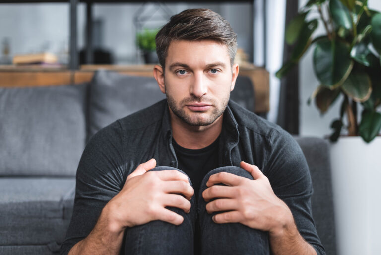 handsome man with panic attack hugging legs in apartment